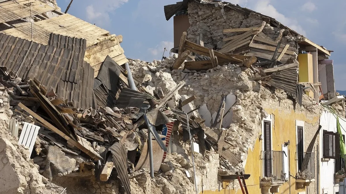 A building that has been severely damaged by an earthquake, with debris scattered everywhere and the structure's walls and roof partially collapsed.